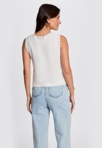 Top nero senza maniche in maglia con scollatura e orlo a onde, abbinato a jeans azzurri a vita alta con tasche posteriori.