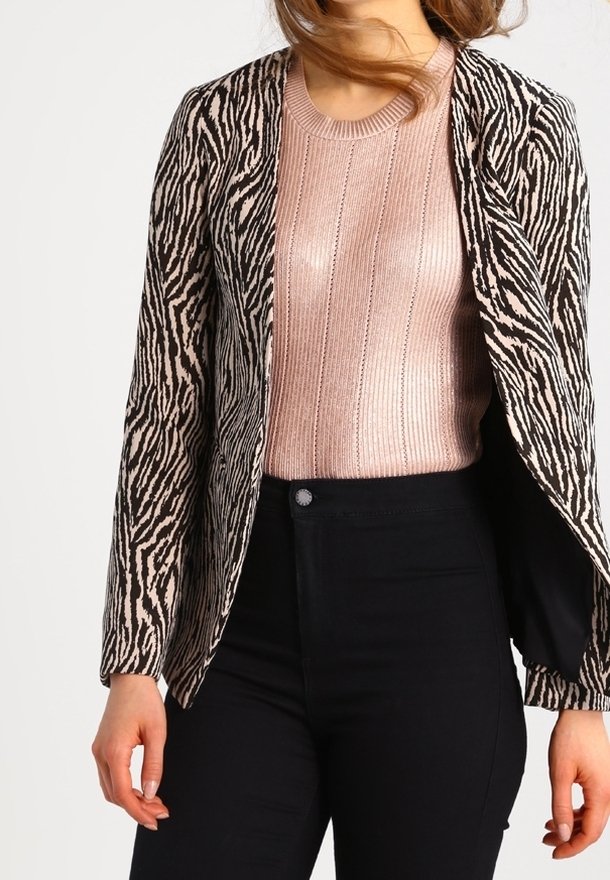 Blazer à imprimé zèbre noir et beige à coupe ample, associé à un pull côtelé rose clair. Un pantalon noir complète la tenue.