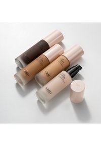 Quatre flacons de fond de teint liquide KIKO Milano Love Fusion en différentes teintes allant du foncé au clair, dont un avec une pompe ouverte et son bouchon à côté.