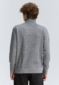 Pulover gri cu guler înalt, model texturat, mâneci lungi și manșete și tiv cu nervuri, asortat cu blugi negri.