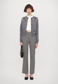 Szürke kardigán virágmintás hímzéssel, fehér crop top, fekete-fehér mintás nadrág és egy fekete kézitáska. Az öltözéket lapos fekete cipők egészítik ki.