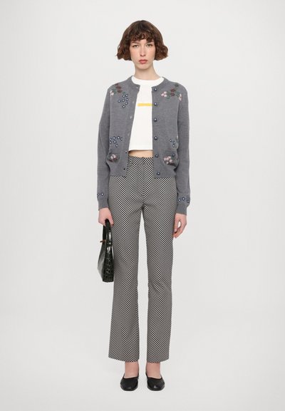 Szürke kardigán virágmintás hímzéssel, fehér crop top, fekete-fehér mintás nadrág és egy fekete kézitáska. Az öltözéket lapos fekete cipők egészítik ki.