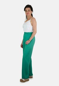 Pantalones verdes de pierna ancha hechos de una tela suave, con una cinturilla elástica, combinados con una blusa blanca de tirantes spaghetti y sandalias de cuña de color claro.