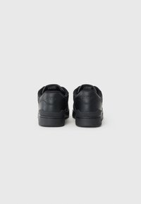 Black leather sneakers with a smooth texture, rounded shape, and padded collar. Features embossed logo on the heel and contrasting sole.