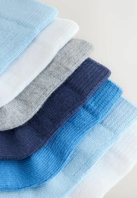 Stapeltje opgevouwen katoenen sokken in tinten blauw, marineblauw, grijs en wit, diagonaal gerangschikt op een wit oppervlak.