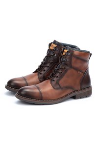 Pareja de botas de tobillo de cuero marrón con cordones, con punteras de color marrón oscuro y paneles laterales texturizados sobre fondo blanco.