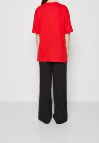 Červené oversize tričko s krátkým rukávem a kulatým výstřihem, kombinované s černými širokými kalhotami se bílými bočními pruhy.
