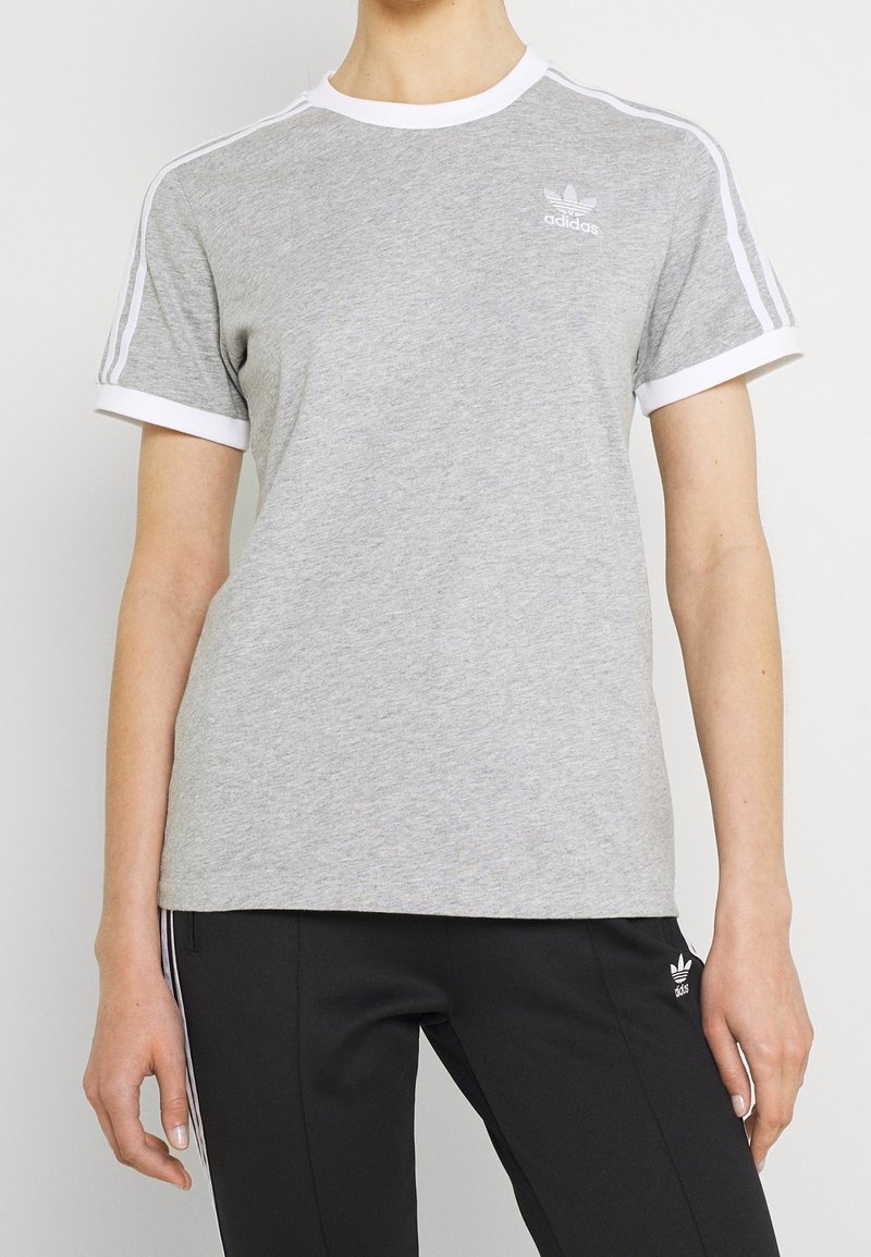 Šedé bavlněné tričko s bílým žebrovaným límcem a manžetami, se třemi bílými pruhy na ramenou a malým logem na hrudi.