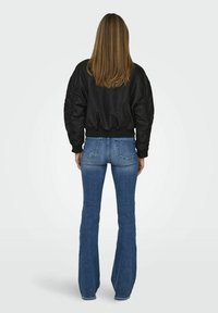 Veste bomber noire avec des manches texturées, associée à un jean bleu évasé. Les deux vêtements sont présentés de dos, mettant en avant la forme et l'ajustement.