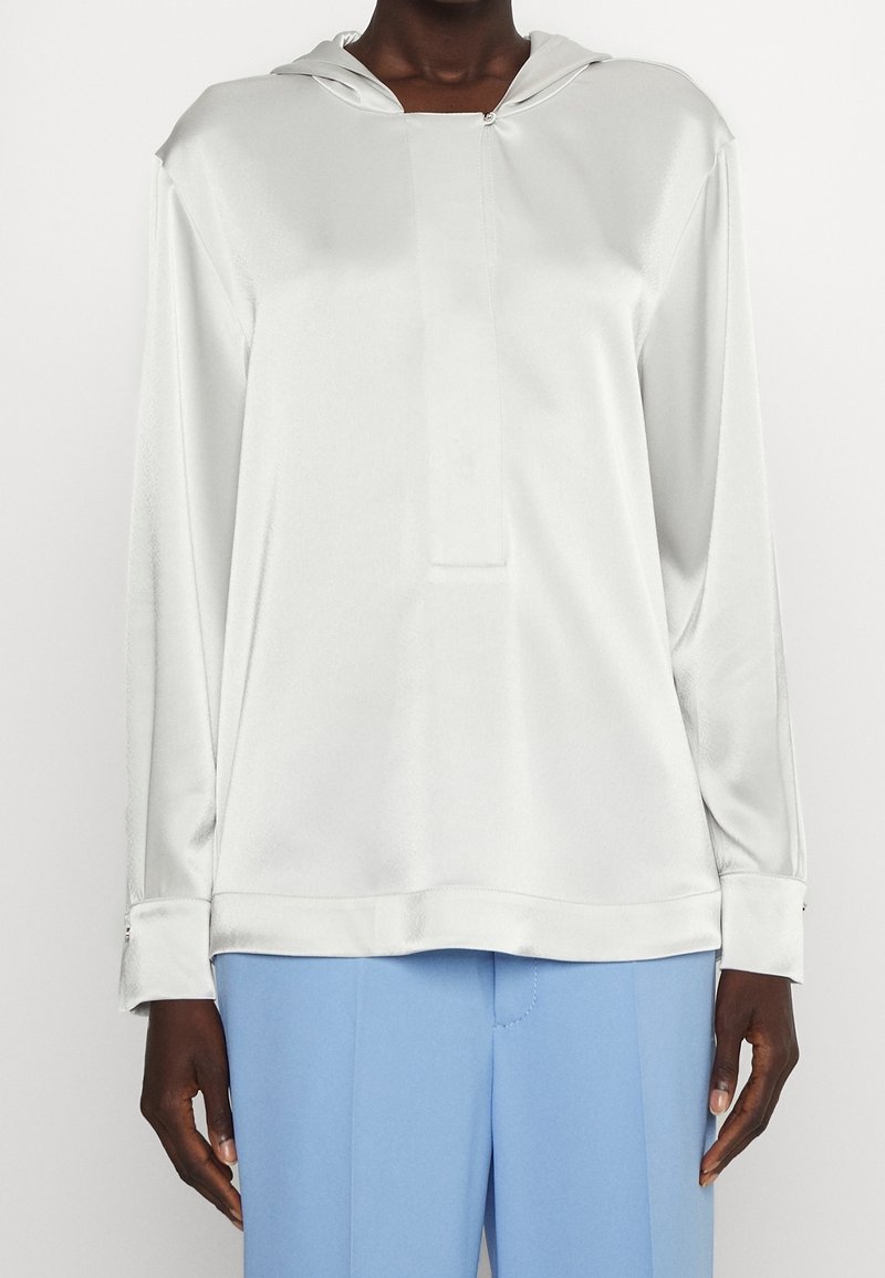 White satin long-sleeve top with a hood and a front placket. Features cuffs with button details, paired with light blue tailored pants.