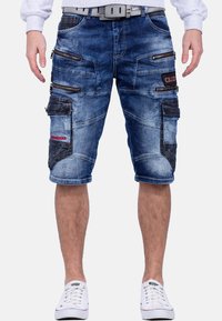 Shorts cargo en denim déchiré bleu avec plusieurs poches zippées et une coupe décontractée. Présente des coutures contrastées et une ceinture.