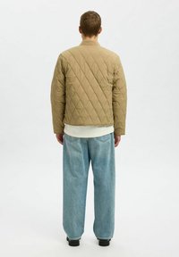 Kurtka bomber w kolorze jasnobrązowym, pikowana, z okrągłym kołnierzem, z diamentowym wzorem i luźnym krojem, w połączeniu z jasnoniebieskimi, szerokimi dżinsami.
