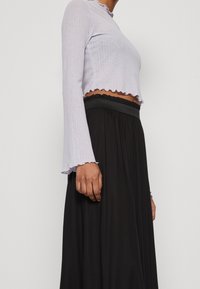 Lichtpaarse cropped top met een golvende zoom en lange mouwen, gecombineerd met een zwarte rok met hoge taille en een elastische tailleband.