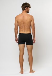 Boxeri negri dintr-un material neted, având un elastic cu brand. Designul este ajustat și are o lungime până la mijlocul coapsei.