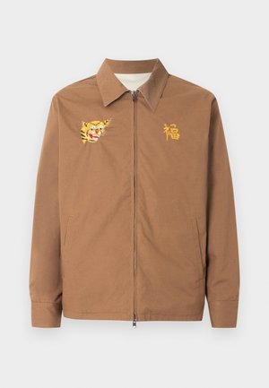 Veste marron zippée avec col, avec une tête de tigre jaune brodée sur la poitrine gauche et un caractère chinois jaune sur la poitrine droite.