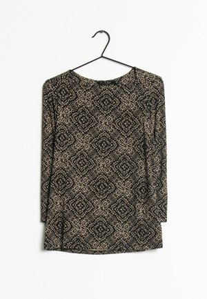 Haut noir à manches longues avec motif à points géométriques beige suspendu sur un cintre noir sur fond blanc.