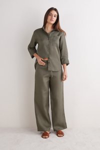 Olivengroene linnen overhemd met knoopsluiting en een borstzak, gecombineerd met brede bijpassende broek en bruine sliders.