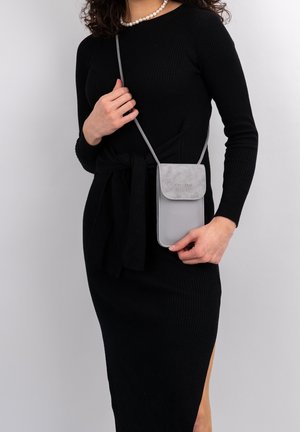 Borsa a tracolla grigia realizzata in pelle e suede, con chiusura a pattina, design minimalista e tracolla sottile. Indossata con un vestito nero.