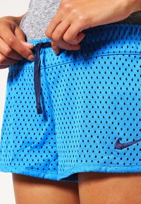 Blå perforerade sportshorts med dragsko i midjan, med en liten lila Nike-logotyp på sidan. Texturerad tyg för andningsförmåga.