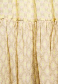 Jasnożółty materiał o geometrycznym wzorze, z rombami w delikatnym różu i kremie. Tekstura wydaje się gładka z zebranymi fałdami.