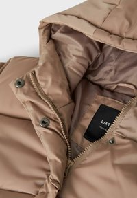 Beige quiltad puffer-jacka med huva, med dragkedja framtill, tryckknappar och en intern ficka för etikett. Slät innervaddering.