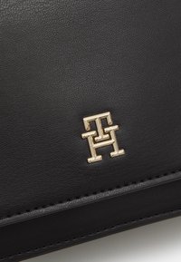 Czarny skórzany woreczek z teksturowaną powierzchnią i złoconym logo na środku. Starannie zszyte krawędzie.