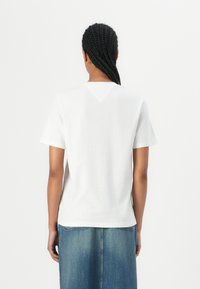 T-shirt en coton blanc à manches courtes, avec un décolleté en V à l'arrière, associé à une jupe en jean bleu.