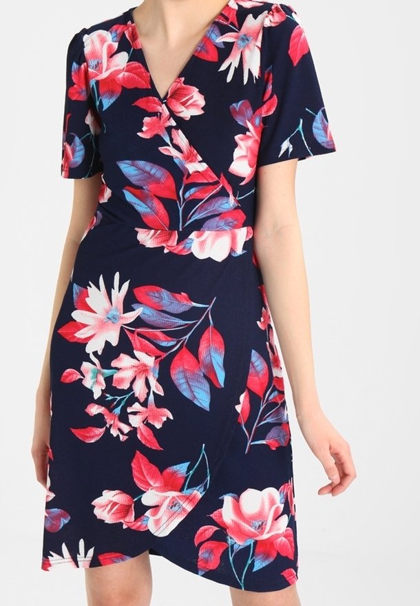 Femme portant une robe bleu marine longueur genou avec des motifs floraux rouges, roses et bleus et des manches courtes.