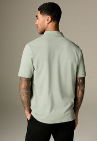 Lys grøn kortærmet polo-shirt med klassisk krave, glat tekstur og en afslappet pasform, der har diskrete stikningsdetaljer.