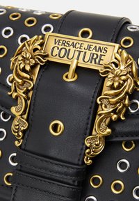 Borsa in ecopelle nera con borchie metalliche in oro, argento e bianco. La chiusura presenta un decoro in tono oro con logo.