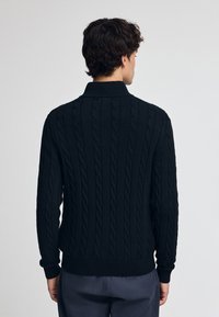 Pull en maille torsadée noir avec un col haut et des poignets côtelés, présentant un motif texturé sur l'ensemble du tissu. Design simple et ajusté.