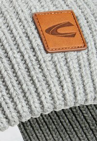 Graue Strickmütze mit einem strukturierten Rippmuster und einem braunen Lederpatch mit geprägt Logo. Weiches und flexibles Material.