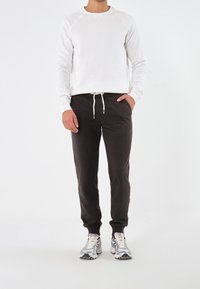 Weißes Sweatshirt mit Raglanärmeln, kombiniert mit schwarzen Jogginghosen mit einem Kordelzugbund. Die Schuhe sind silber mit bunten Akzenten.