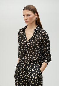 Black sheer shirt with cream abstract dots, buttoned down, paired with matching high-waisted trousers. Smooth texture, relaxed fit.