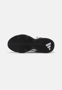 Semelle de chaussure noire avec des motifs circulaires et en chevrons, avec un logo Adidas blanc près du talon sur un fond gris clair.
