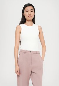 Haut sans manches blanc avec un col rond associé à un pantalon rose clair avec poches latérales et une fermeture à boutons à l'avant. Tissu en maille lisse.