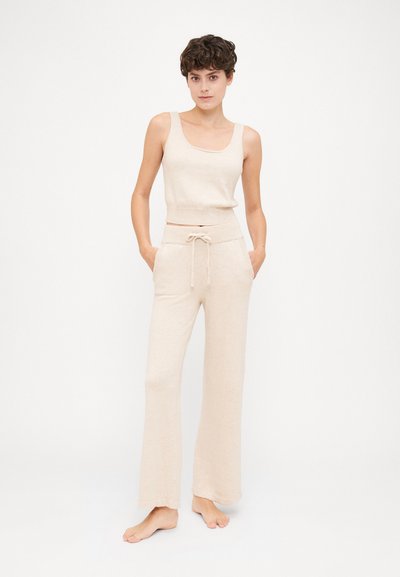 Μπεζ πλεκτό τοπ tank με φαρδιά λαιμόκοψη σε συνδυασμό με αντίστοιχα φαρδιά παντελόνια με κορδόνι στη μέση. Το υλικό φαίνεται μαλακό με μια διακριτική υφή.