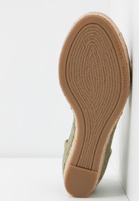 Semelle d'une espadrille verte avec motif tissé et talon en caoutchouc marron, marquée "Tommy Hilfiger" sur le côté.