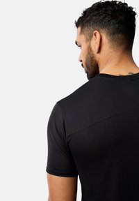 Svart idrottströja tillverkad av ett glansigt, elastiskt tyg, med rund halsringning och korta ärmar, som har subtila texturer och design detaljer.