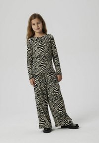 Outfit con stampa zebra composto da un top a maniche lunghe e pantaloni a gamba larga. Realizzato in tessuto morbido, con audaci strisce nere e beige. Scarpe nere.