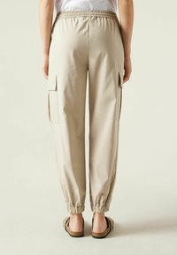Beige cargo kalhoty s šňůrkovým pasem a elastickými manžetami. Obsahují boční kapsy a hladkou texturu látky.