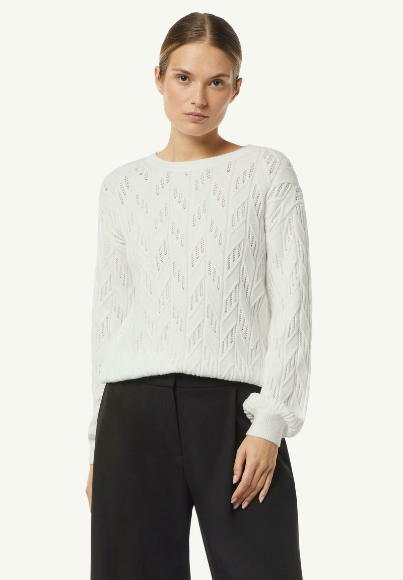 White knitted sweater with diamond pattern, round neck, and ribbed cuffs. Paired with black high-waisted trousers for a layered look.