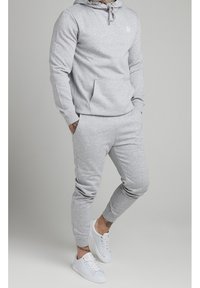 Sudadera de algodón gris con cordón y bolsillo frontal, combinada con pantalones de chándal estrechos a juego. Completado con zapatillas blancas.