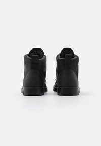 Botas negras al tobillo hechas de cuero suave, con un interior forrado de material blando, puntera redondeada y suelas de goma resistentes. Lengüeta en la parte trasera para ponerlas y quitarlas con facilidad.