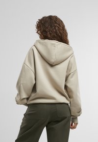 Beige hoodie met verlaagde schouders en geribde manchetten, gecombineerd met donkergroene broek. Soepele, zachte stof met een relaxte pasvorm.