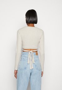 Top crop de mangas longas cinza claro com textura canelada e detalhe nas costas amarrado, combinado com jeans de cintura alta em denim azul claro.