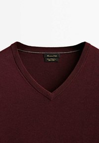 Bordeaux v-hals trui gemaakt van zacht breiwerk, met geribbelde details bij de halslijn en een gladde textuur. Etiket zichtbaar aan de binnenkant.