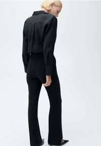 Černá košile na knoflíky vyrobená z texturované tkaniny, spárovaná s přiléhavými černými kalhotami s rozšířenými nohavicemi. Oba kousky mají minimalistický design a čisté linie.