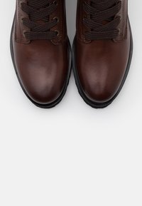 Stivali in pelle marrone con lacci scuri, con una finitura liscia e punte arrotondate. Le suole sono in gomma nera con una leggera tassellatura per una migliore aderenza.