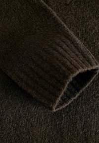 Tissu tricoté texturé marron foncé avec une manche côtelée. Le matériau semble doux et épais, mettant en avant un design confortable et chaud.
